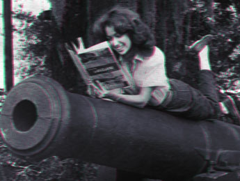 Une jeune fille lit allongée sur un canon militaire.